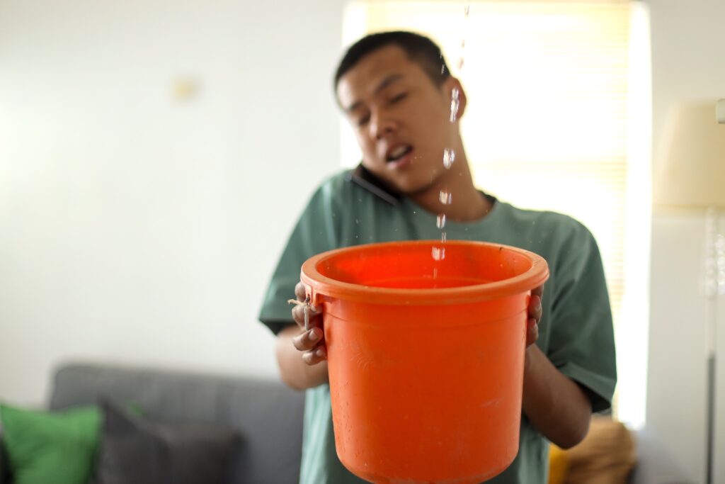 Man holding a bucket as water drips into it
